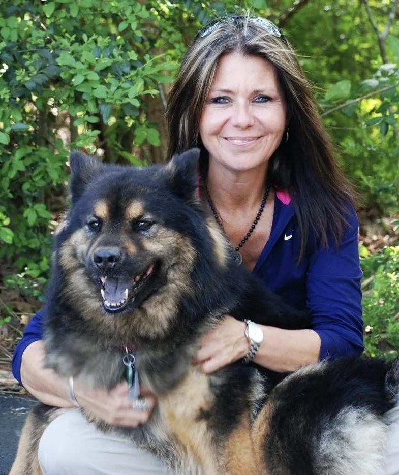Dog psychologist Angie Woods smiling outdoors with her arm around a black and tan dog